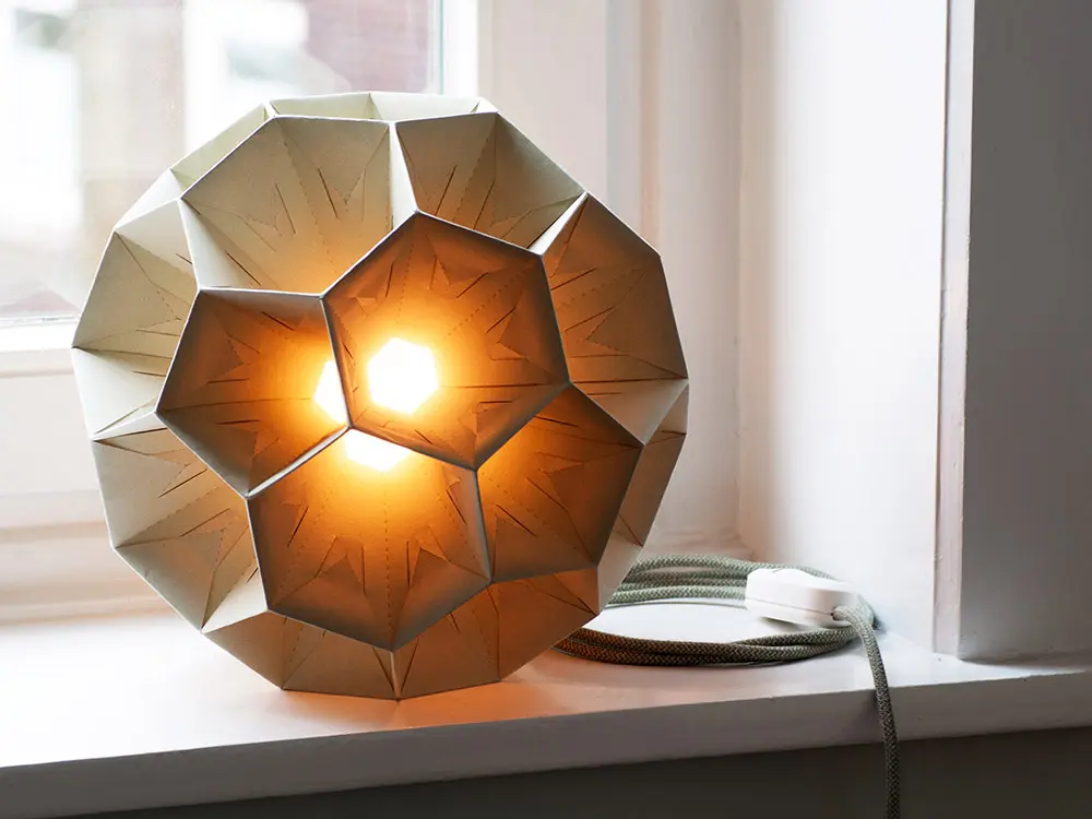 Leuchtende Deckenlampe aus hell-grünlichem Kiwipapier auf der Fensterbank mit warmem Licht.