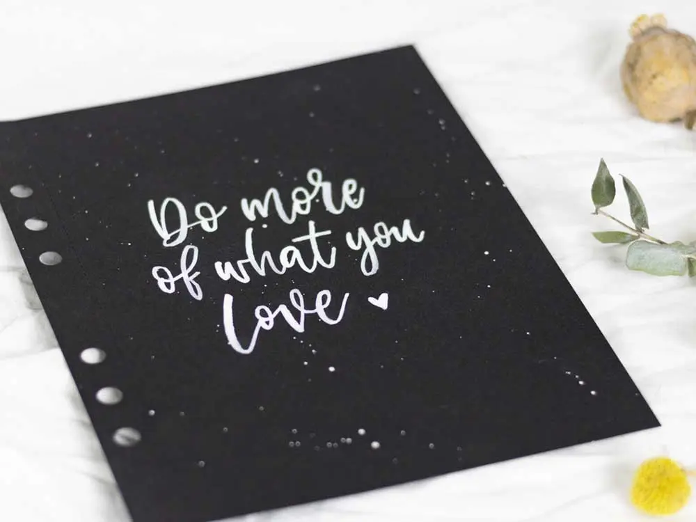 Schwarzes Papier mit Brushlettering-Schriftzug „Do more of what you love“ in Weiß von Martina Johanna Janssen