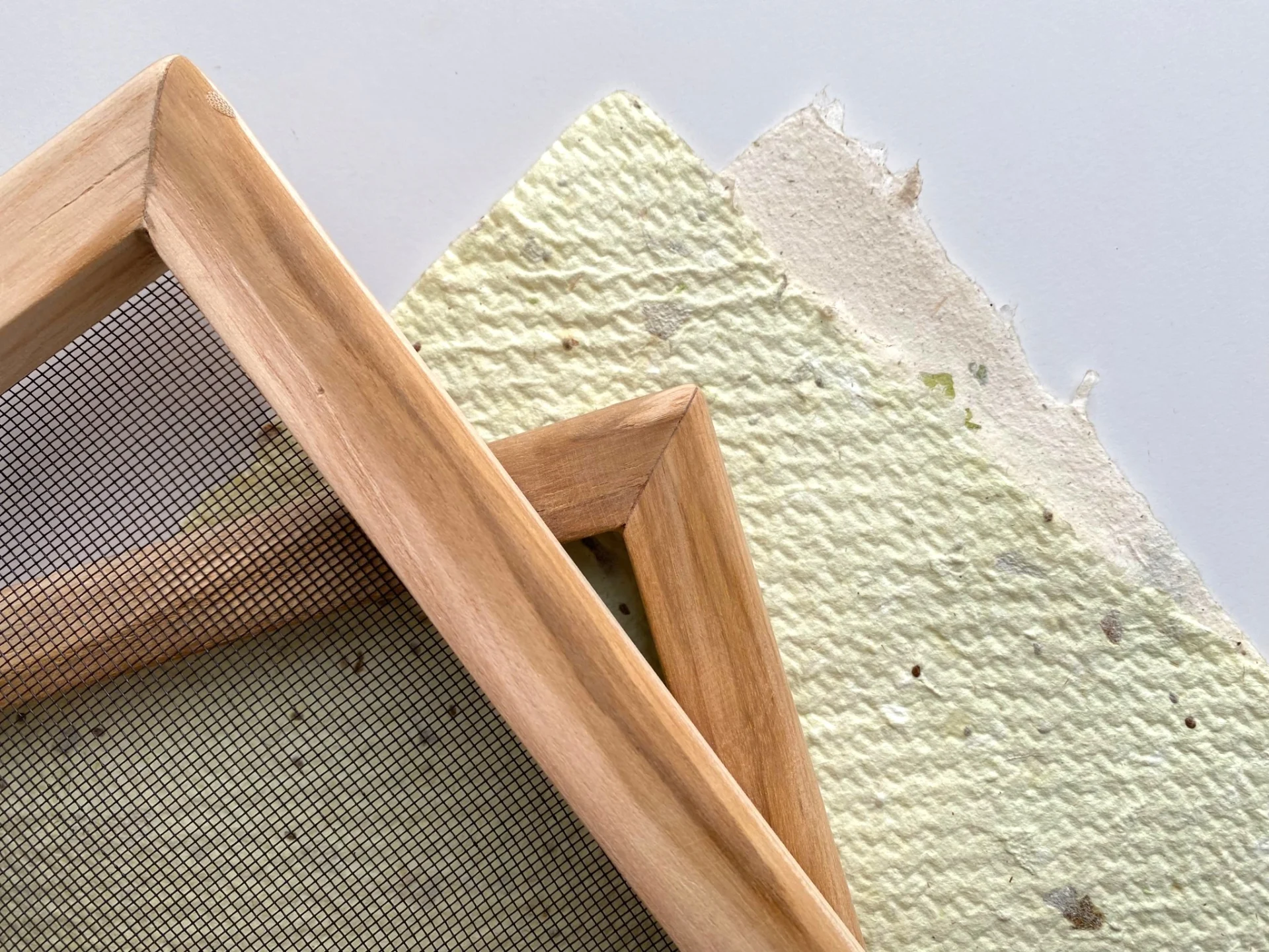 A6 Papierschöpfrahmen aus Holz neben selbst geschöpftem Büttenpapier mit echten Blüten und Naturfasern